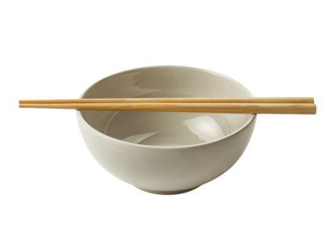  A plain, light-colored ceramic bowl sits with a pair of wooden chopsticks resting horizontally across its rim. 