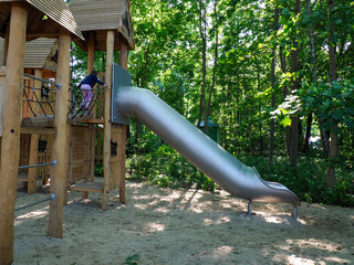 Sunny view of an empty modern wooden playground structure with a long slide and sand base in a forest park