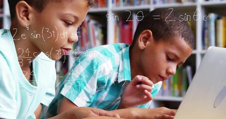 Studying two boys solving math problems in study room, with laptop and bookshelves with books