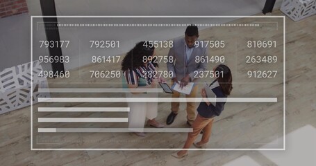 Three team members wearing business attire analyzing data in open office, with tablet clipboard pen