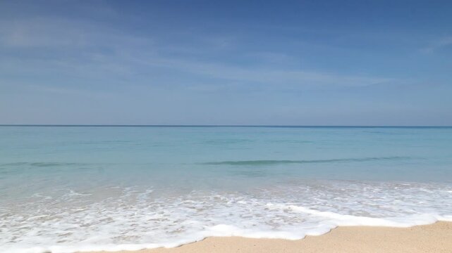 A serene beach scene unfolds, with gentle waves caressing the shore under a clear, azure sky, capturing the essence of tranquility and the allure of a perfect coastal day.