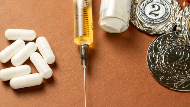 Syringes, medals, and pills on background represent doping in sports. The use of anabolic steroids by athletes for performance enhancement is a form of sports fraud. Doping is a serious issue that