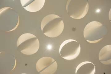 a ceiling adorned with multiple circular cutouts. The ceiling is painted in a soft, cream color, and the circular cutouts are evenly spaced, creating a pattern of light and shadow.