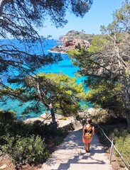 Fashionable girl walking towards to a blue lagoon. Cala Llombards, island Mallorca, Spain, Park near sea with transparent water. Clear turquoise water. Stairs lead to sea.  Summer vacation solo travel