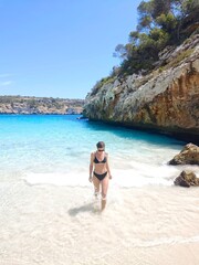 Young slim woman in black bikini comes out of sea, walk on white sand beach, turquoise water and blue sky in background. Active lifestyle, carefree vacation. Solo Model photoshoot. Natural beauty Blog
