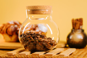 Coffee beans in a clear jar placed on a wooden tray with baked goods in a warm setting