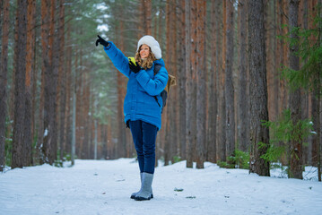 Female hiker dressed in warm winter clothing and carrying a backpack is pointing her finger while navigating a snowy forest trail, embracing the beauty of winter's wilderness