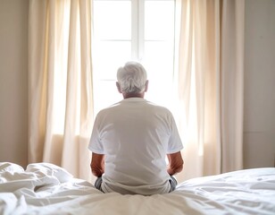 Elderly man sits facing window, contemplative