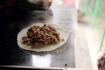 The freshly cooked savory filling for a Lumpia Basah Bogor, a popular Indonesian wet spring roll, sits on a wrapper, ready to be folded at a street food stall.