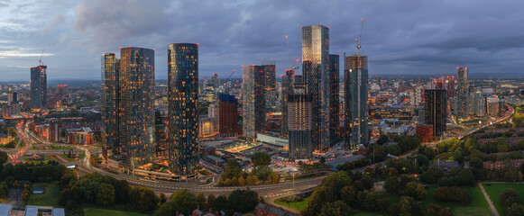 Aerial panoramic view of Manchester skyline at twilight with illuminated towers and Mancunian Way traffic below.