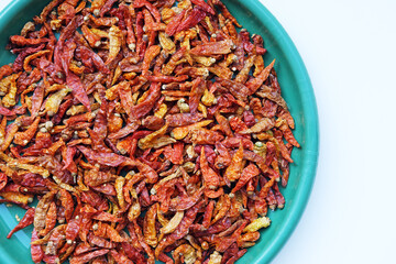 Fototapeta premium A top-down flat lay of dried red chili peppers in a turquoise plastic bowl, isolated on a clean white background with ample copy space.