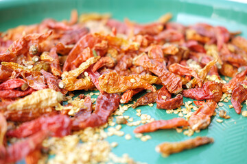 A high-angle view of dried red chili peppers and scattered seeds spread out on a textured turquoise mat, suggesting the process of sun-drying spices.