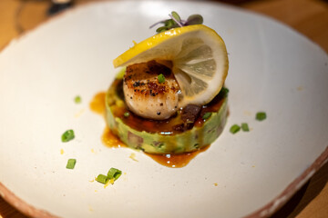 Seared scallops served on plate with avocado and topped with a slice of lemon
