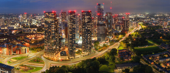Night aerial panorama of Manchester skyline with glowing towers, streetlights, and Mancunian Way traffic below.