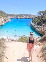 May 12 2024, Calo del Moro, Mallorca, Spain. Fashionable girl posing near a blue lagoon. Viewpoint of beach with transparent water. Clear turquoise water. Summer vacation solo travel. Travel agency