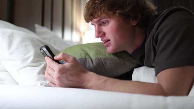 Man lying on bed smiling at smartphone addicted to social media dopamine hits showing digital dependence and modern lifestyle habit in cozy calm bedroom with soft natural light