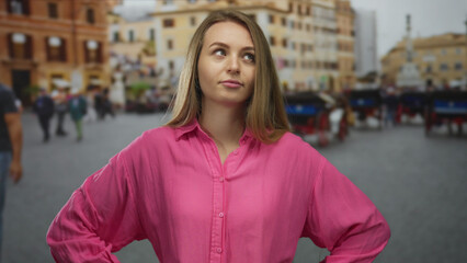 Fototapeta premium Woman standing outdoors in city street wearing pink shirt with closed eyes expressing frustration amidst blurred urban background.