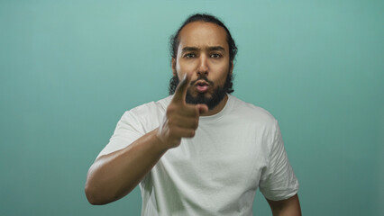Man points finger directly toward camera in studio against teal backdrop, wearing a plain white t shirt; anger confrontation.