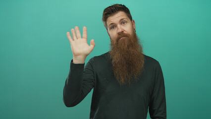 Man with long brown beard raises bare hand with open palm against a teal studio background; curiosity.