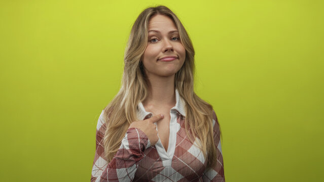 Blonde caucasian woman with gentle smile points finger to chest in studio; self esteem confidence pride.