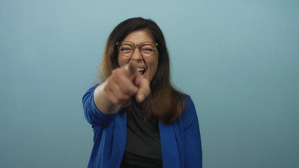 Middle aged hispanic woman wearing glasses pointing finger to camera in studio against light blue...
