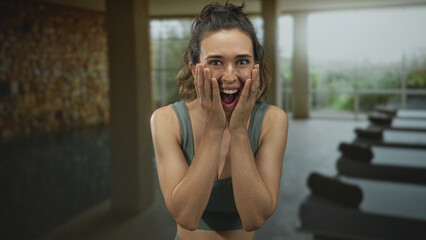 Young woman holds cheeks with hands in modern indoor spa pool building with stone wall and yoga...