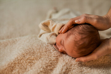 An awake infant wearing a cozy, knitted cream outfit and bonnet, lying on its back on a plush, neutral-colored blanket. Perfect for newborn photography