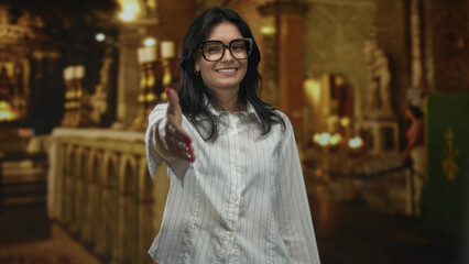 Woman wearing white shirt extends hand for handshake in building; welcome goodwill fellowship faith.