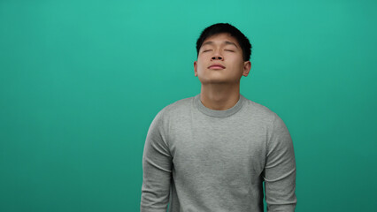Young man with closed eyes wearing gray sweater against green background expressing tranquility and contentment in a minimalist setting.