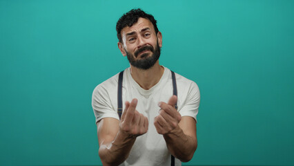 Hispanic man with beard gesturing for begging against a green background, wearing a white shirt and...