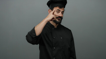 Fototapeta premium Hispanic male chef in black uniform gestures thoughtfully against grey backdrop, suggesting innovation in culinary arts.