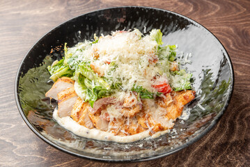 Grilled chicken Caesar salad with romaine lettuce, cherry tomatoes, croutons, Parmesan cheese, and creamy dressing served on a black plate over rustic wooden background.