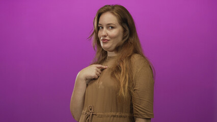 Young caucasian woman wearing brown dress pointing finger to chest against vibrant purple studio backdrop; confidence.