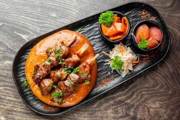 Grilled meat skewers on flatbread with sauce, pickled vegetables, and cabbage salad. Gourmet presentation on black plate. Top view, restaurant-style serving.