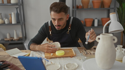 Man shaping clay bowl with bare hands on wooden table in artisan workshop with pottery shelves;...