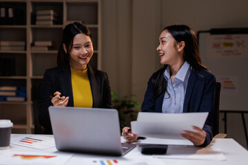 In a dimly lit office, business asian women collaborate late into the night. This image captures the intensity and focus of teamwork necessary for project success.
