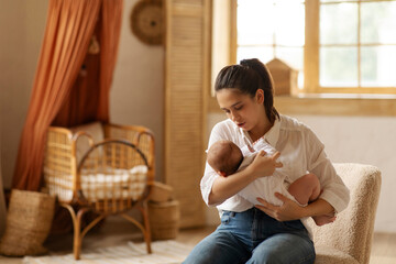 Growth spurt and teething concept. Caring mother holding and calming her baby on hands, sitting on...