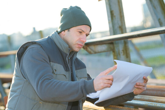 middle-aged manual worker wearing beanie hat looking at paperwork
