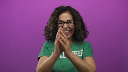 Woman volunteer in green uniform happily clapping with a joyful expression against an isolated pink background