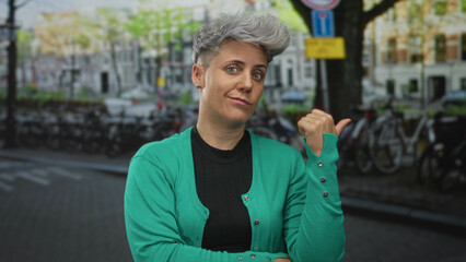 Woman with short hair wearing green cardigan hand pointing to bicycles on city street lined with...