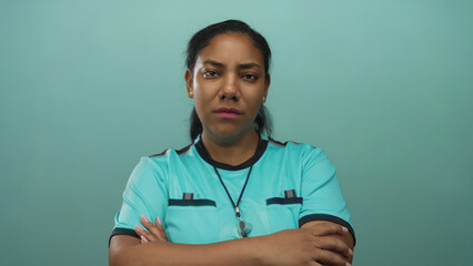 African american woman referee grips whistle and crosses arms with furrowed brow in studio; determination.