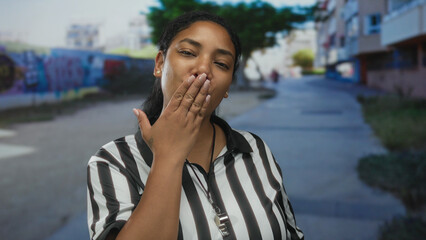 Referee woman puckering lips to blow kiss while holding whistle in striped shirt on a street;...