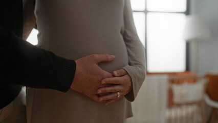 Pregnant woman with partner in home nursery touching belly, showcasing anticipation and love, highlighting gentle connection in cozy room.