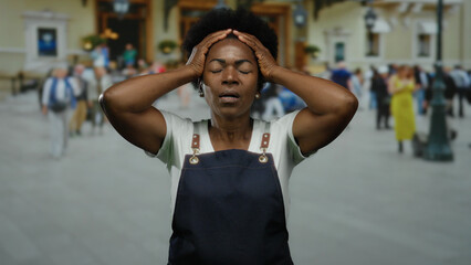 Obraz premium Woman in apron standing on busy city street with hands on head, expressing stress, surrounded by people and urban setting, conveying everyday challenges of urban life.