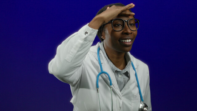 Woman doctor smiling against blue background with stethoscope wearing white coat and glasses featuring isolated professional healthcare provider adult black female medical.