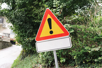 Warning road sign with exclamation mark and empty white plate. Concept of alert, attention and safety message. Traffic warning symbol on green roadside background. © Paweł Michałowski