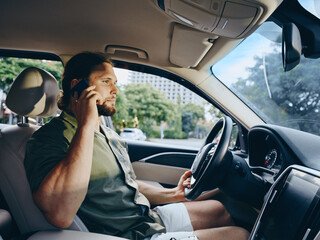 A bearded man sits behind the wheel of a modern car, speaking on a mobile phone while driving, conveying focus, concentration, and a casual travel mood.
