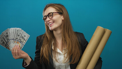 Woman with glasses and brown hair holds dollar bills and cardboard tubes against teal wall in...