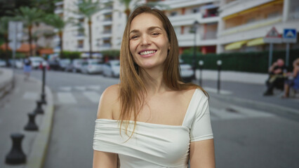 Woman bare shoulder smiling in white top under warm sunlight on urban street scene with blurred...