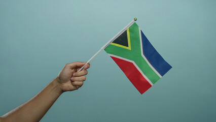 Hand holding south african flag against a blue background symbolizes patriotism and cultural pride,...